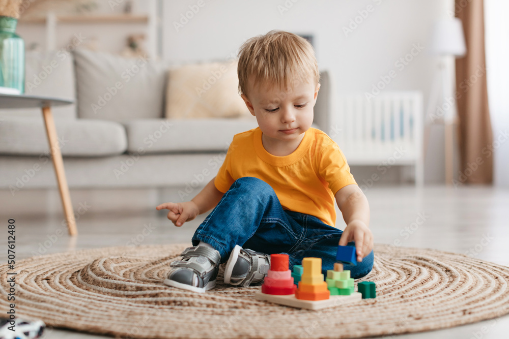 Early development concept. Little toddler boy playing with educational wooden toy at home, sitting in living room - obrazy, fototapety, plakaty 