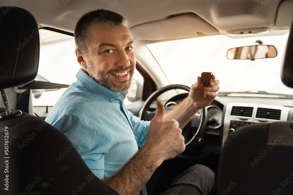 Happy man sitting in car showing keys gesturing thumbs up
