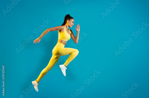 Sportswoman Jumping In Mid Air Exercising Over Blue Background