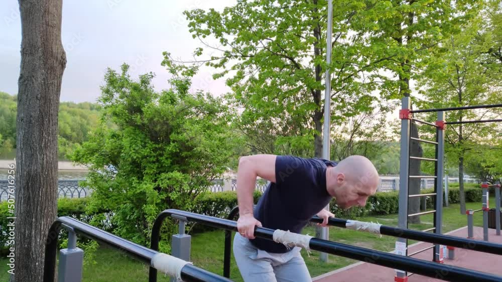 White Caucasian man trains on an outdoor sports field. Man doing gymnastics on parallel bars. Handsome bald man doing push-ups. Outdoor workout. Healthy lifestyle White Caucasian man trains on an outdoor sports field. Man doing gymnastics on parallel bars. Handsome bald man doing push-ups. Outdoor workout. Healthy lifestyle
