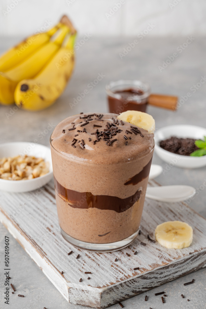 Vegan banana chocolate ice cream with chocolate glaze and sprinkles in a glass on a gray concrete background. Healthy food. Copy space. Vegan banana chocolate ice cream with chocolate glaze and sprinkles in a glass on a gray concrete background. Healthy food. Copy space.