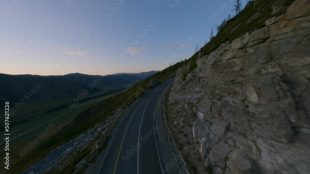 Aerial view empty serpentine asphalt road highway on mountain summit darkness cliff stone texture at natural valley. FPV sports drone shot sunset rocky landscape picturesque hilly terrain forest trees Aerial view empty serpentine asphalt road highway on mountain summit darkness cliff stone texture at natural valley. FPV sports drone shot sunset rocky landscape picturesque hilly terrain forest trees