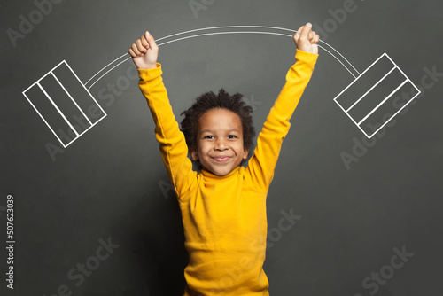 Funny strong black kid with barbell in her hands on chalkboard background photo