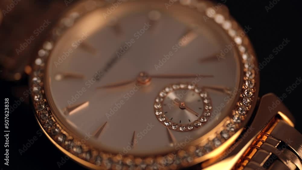 Women's wrist watch. Gold wrist watch with rhinestones and a gold bracelet on a black background. Status accessory. The second hand is accelerated several times.