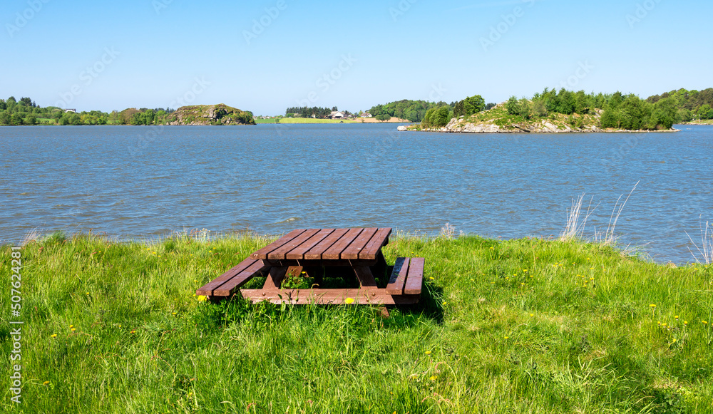 A wooden picnic table with benches on a small grass lawn at Halandsvatnet lake, Stavanger, Norway, May 2018