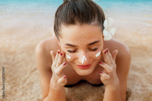 Suntan lotion woman applying sunscreen solar cream. Beautiful happy cute woman  applying suntan cream from a plastic container to her nose with ocean in background. photo