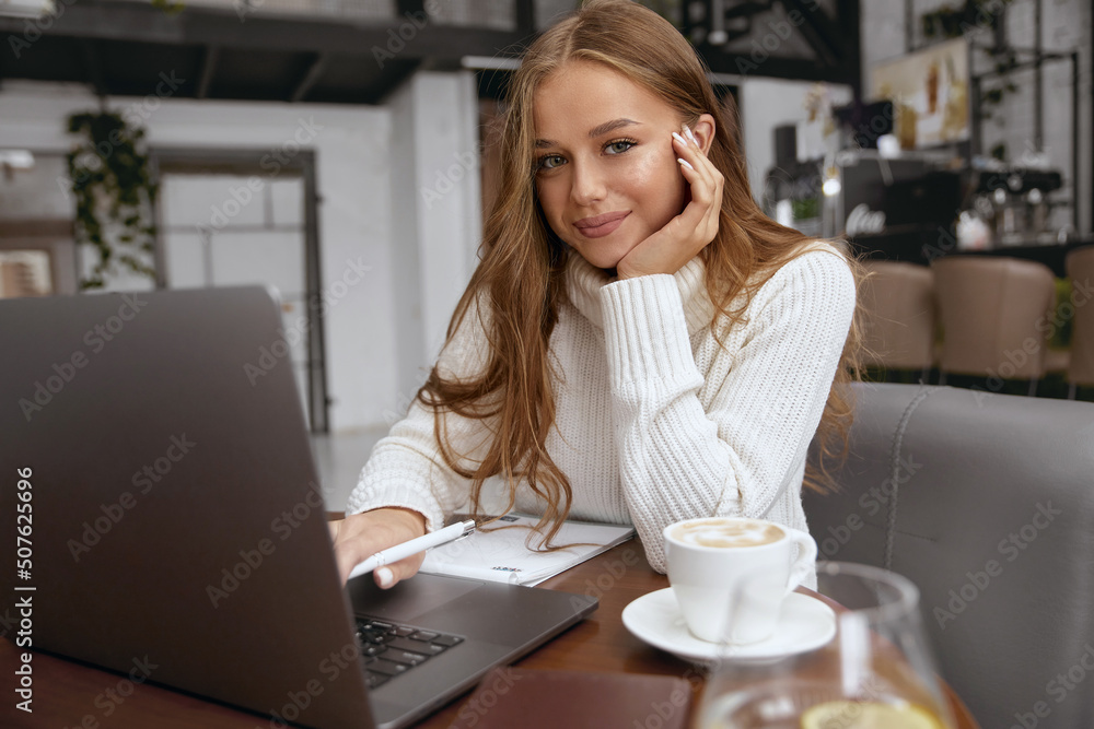 Beautiful woman sitting at table studying using laptop reading a book, surfing internet Beautiful woman sitting at table studying using laptop reading a book, surfing internet
