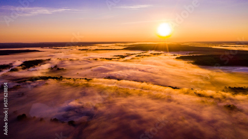 Aerial view of a beautiful summer landscape with a fog while dawn. Photo from drone of a foggy landscape in spring. Top view to land while sunrise. Sun is above the horizon