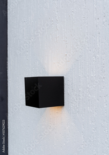 Miniature ice lamp on the wall of the house, facade lighting on the white wall, designer lamp of street lighting of the house, illumination of the building with warm light. © Aleksey