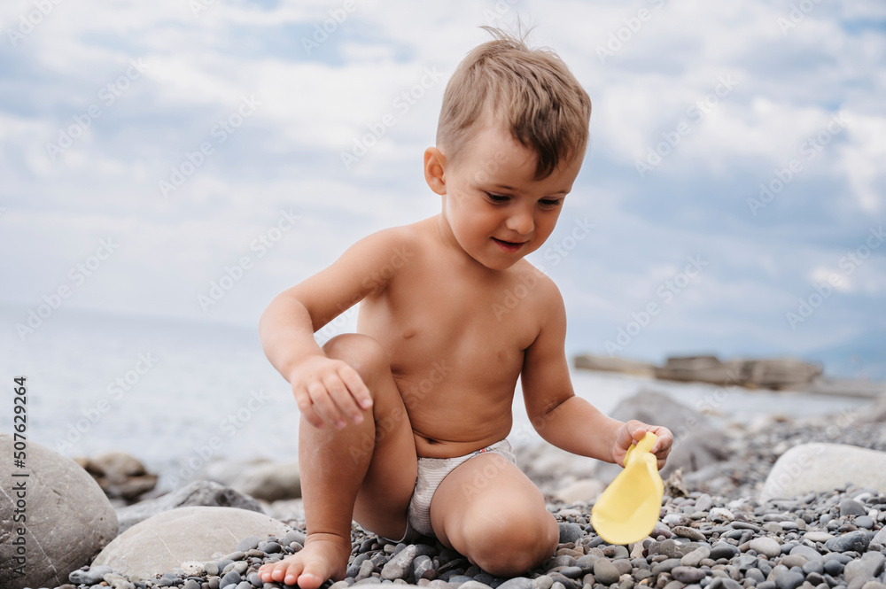 Cute Caucasian boy playing on a pebble beach with a plastic toy. Active holidays on the coast Cute Caucasian boy playing on a pebble beach with a plastic toy. Active holidays on the coast