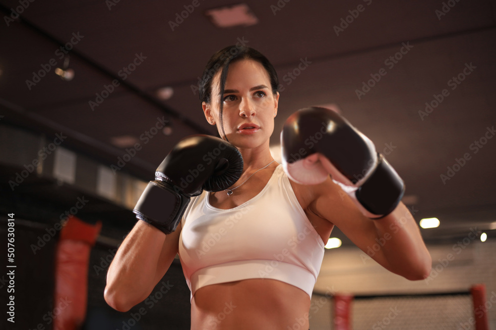 Female in boxing gloves and sportive wear stands in a rack in the boxing hall