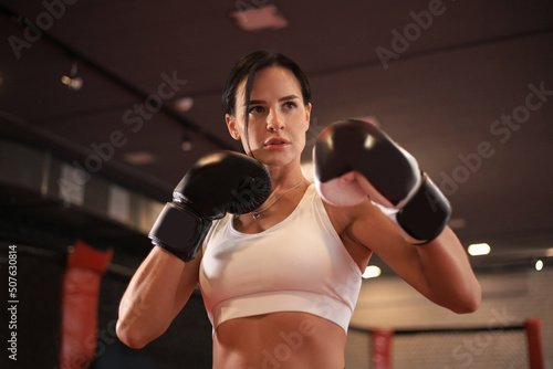 Female in boxing gloves and sportive wear stands in a rack in the boxing hall © ty