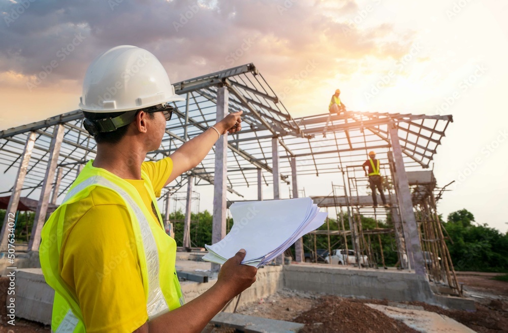 Asian engineer manager, foreman, or leader pointing to home construction structure on workplace while worker working on. Teamwork, Leadership concept. Asian engineer manager, foreman, or leader pointing to home construction structure on workplace while worker working on. Teamwork, Leadership concept.