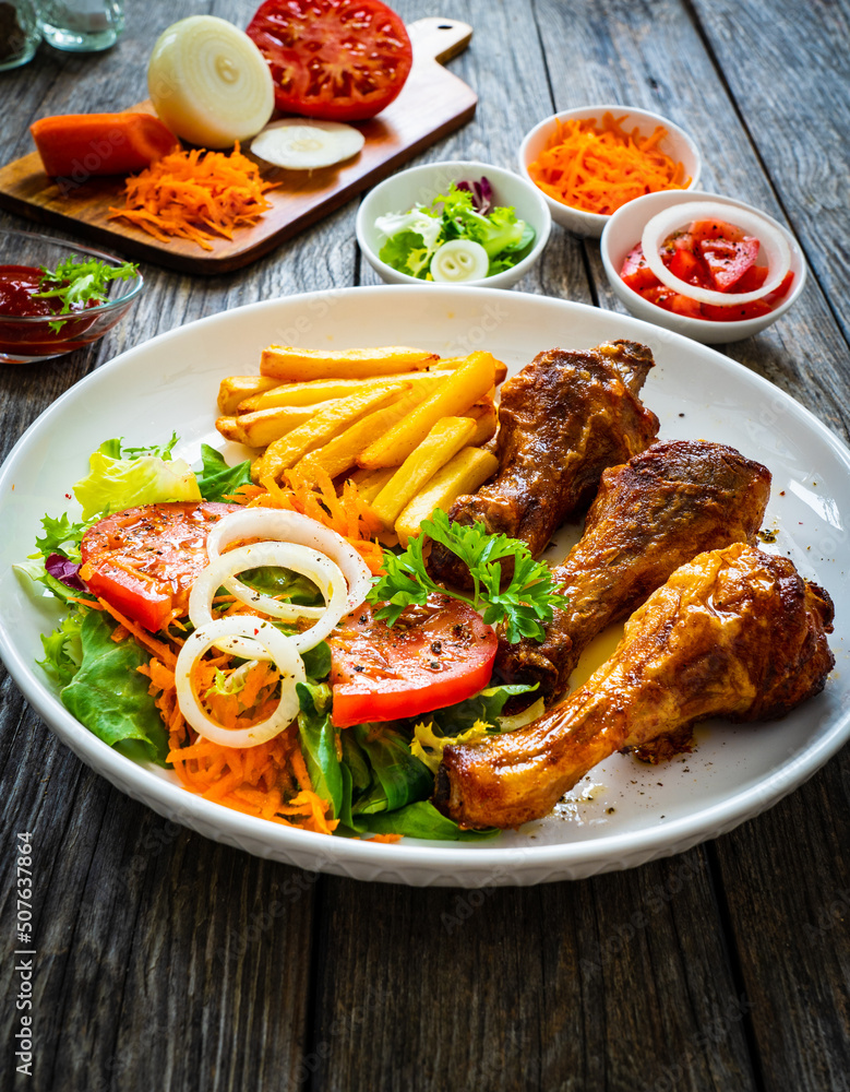 Barbecue chicken drumsticks with chips and greens on wooden table
