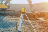 Rotating laser surveying equipment set on construction site with excavator digging foundation in the background.  Laser level as a key device to level construction site