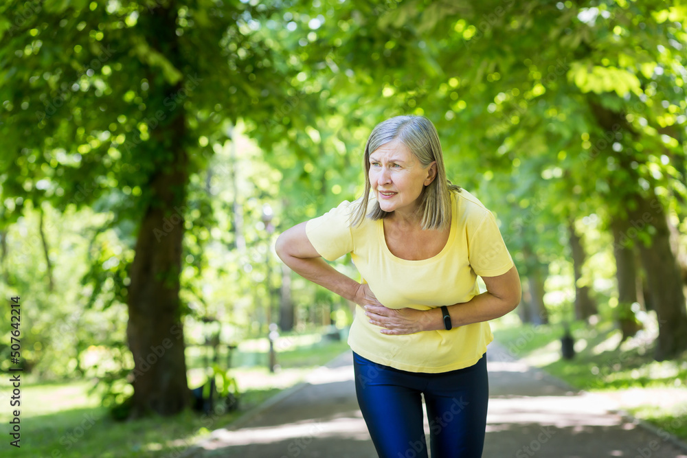 Senior beautiful woman running in the park, playing sports. Her stomach began to ache, she held on to her stomach, bent over in pain. Senior beautiful woman running in the park, playing sports. Her stomach began to ache, she held on to her stomach, bent over in pain.