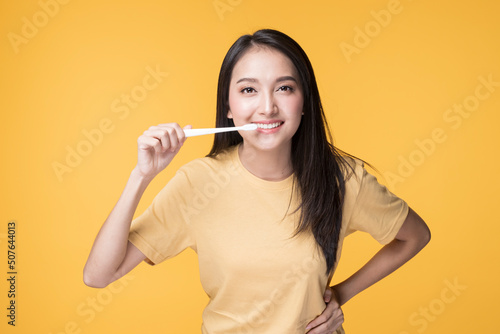 Portrait of Happy Asian female brushing her Teeth. Young Asian Woman brushing her teeth with clean white teeth. Happy Asian Woman wearing Yellow T-shirt standing over yellow background.