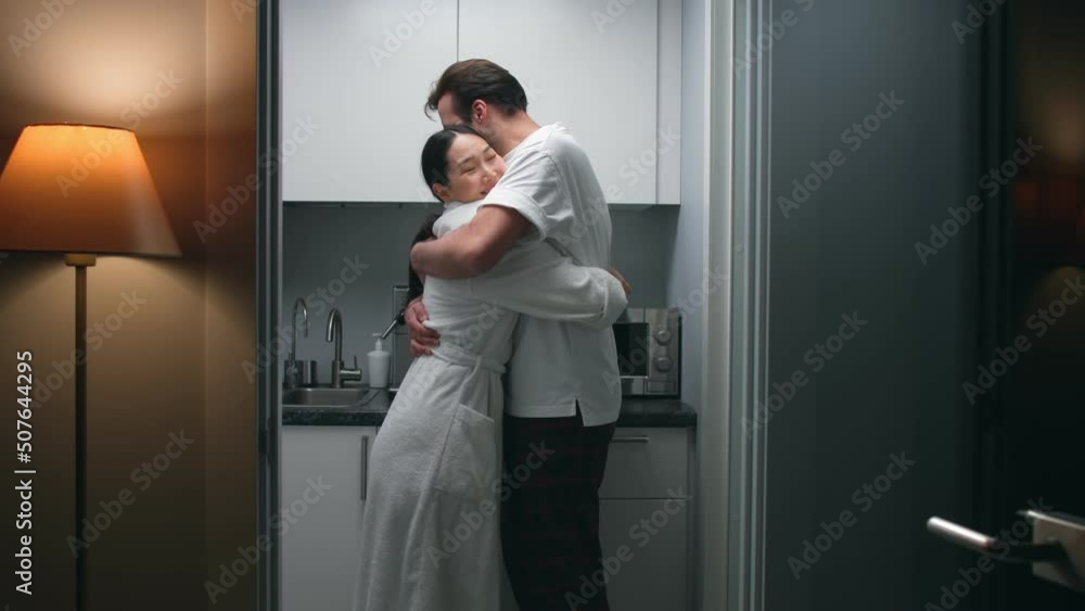 Happy diverse couple in sleepwear hug and smile in small kitchen Happy diverse couple in sleepwear hug and smile in small kitchen