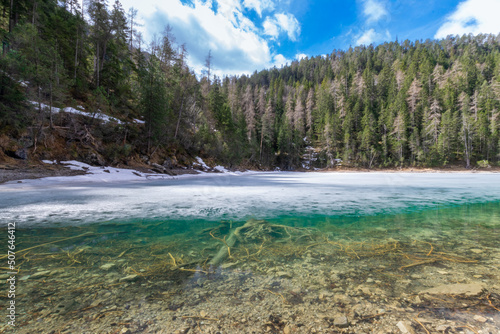 partly frozen, clear mountain lake in the forest during spring (Blindsee, Tyrol, Austria)