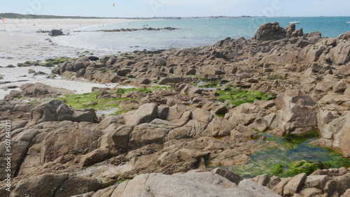 Tas de gros rochers sur la belle plage de Plouédern en Bretagne, avec un mer bleu turquoise, de la végétation maritime verte et des flaques d'eau, et des algues