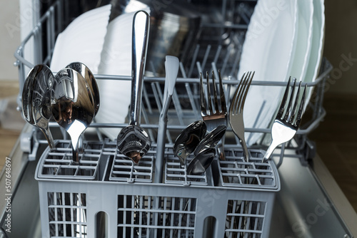 basket with spoons and forks. in the dishwasher. dishwasher. loaded dishwasher. plates, knives, spoons and forks are well washed.