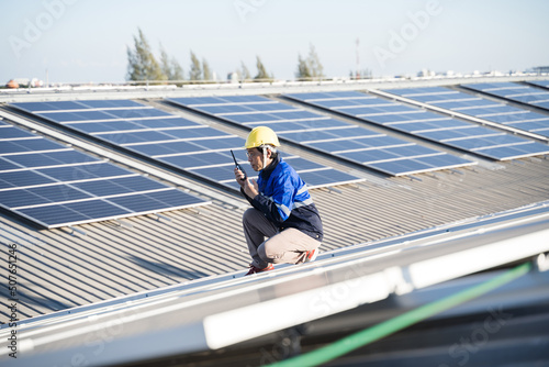 Asian technician installing inspection or repair solar cell panels on background field of photovoltaic solar panels solar cells on roof top factory.