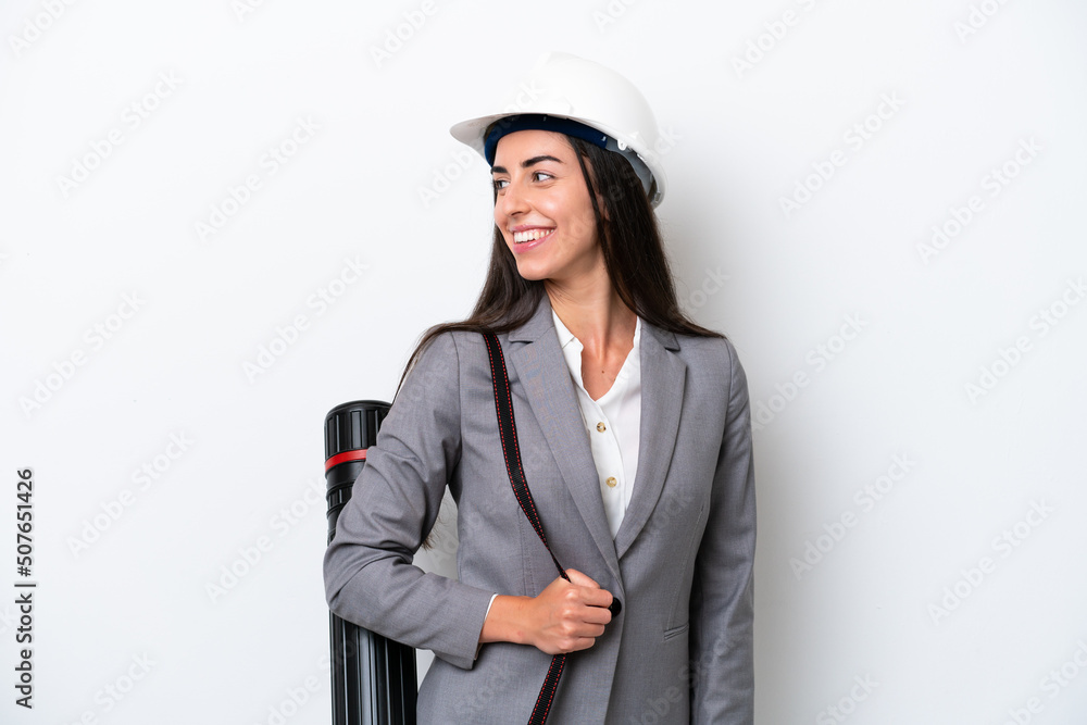 Young architect caucasian woman with helmet and holding blueprints isolated on white background looking side Young architect caucasian woman with helmet and holding blueprints isolated on white background looking side
