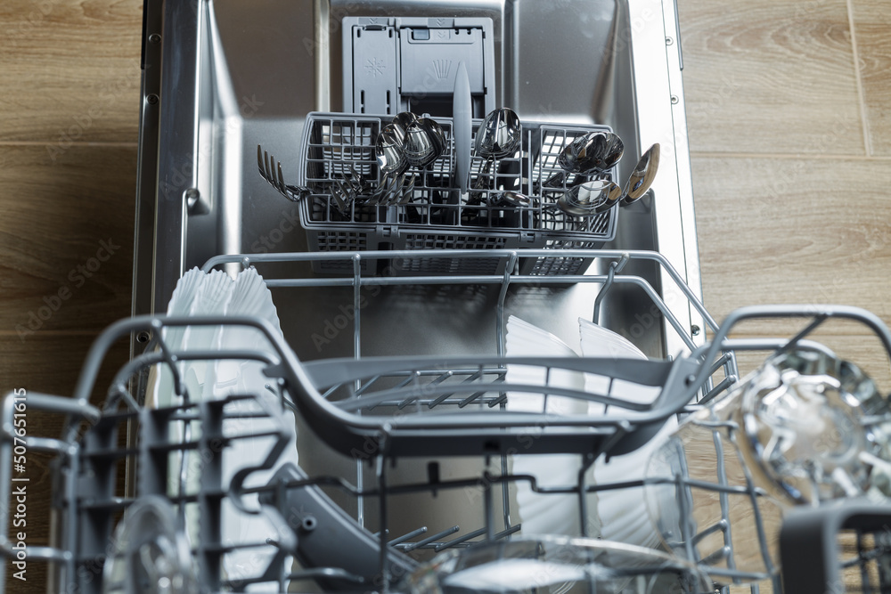 open dishwasher. a basket with spoons and forks stands on the door of the dishwasher. open dishwasher. a basket with spoons and forks stands on the door of the dishwasher.