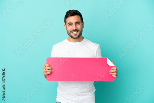 Young handsome caucasian man isolated on blue background holding an empty placard
