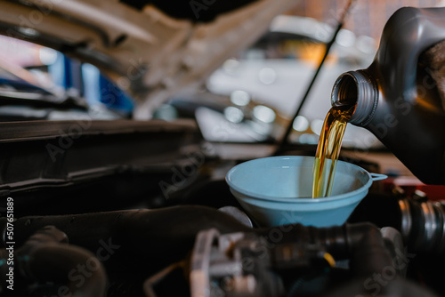 In the car service center the mechanics are filling the engine with new oil for engine maintenance.