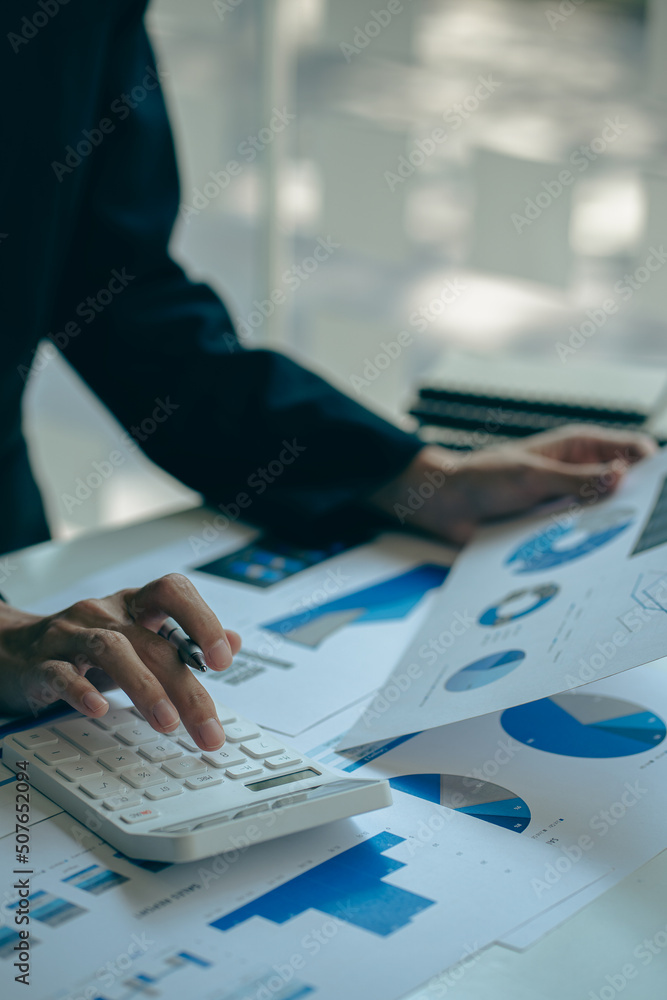 financial concept close-up businessman holding a graph pen press a calculator And make money by writing reports, memos and analyzing vertical image business documents. financial concept close-up businessman holding a graph pen press a calculator And make money by writing reports, memos and analyzing vertical image business documents.