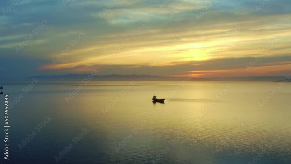 Bulk carrier ship at anchor in orange sunset, aerial view. Bright sunny path on water, red orange sky. Natural landscape. Shipping business sea shipping. Delivery logistics. Panorama from a drone Bulk carrier ship at anchor in orange sunset, aerial view. Bright sunny path on water, red orange sky. Natural landscape. Shipping business sea shipping. Delivery logistics. Panorama from a drone