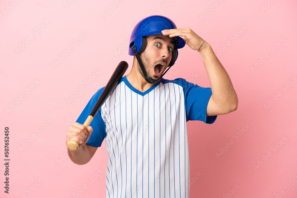 Baseball player with helmet and bat isolated on pink background doing surprise gesture while looking to the side