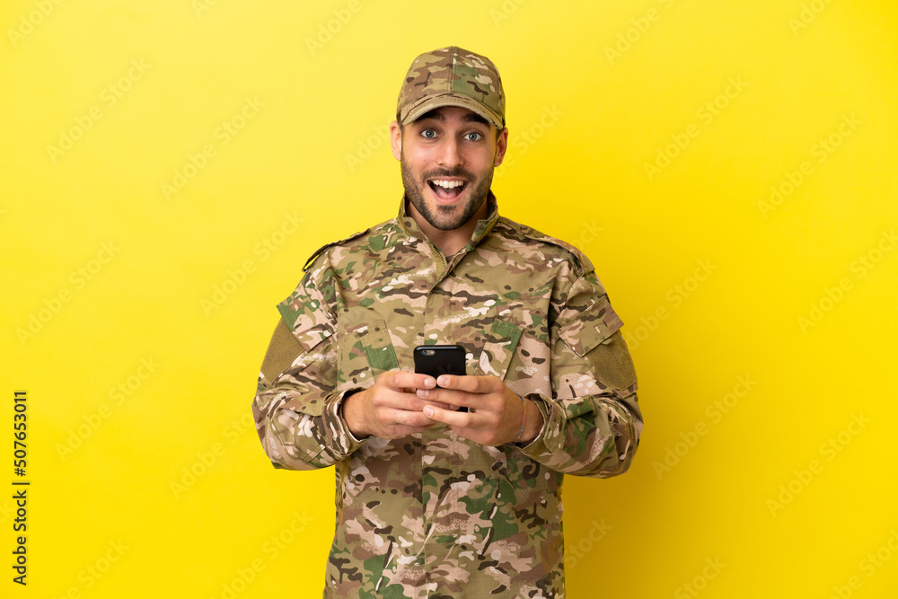Military man isolated on yellow background surprised and sending a message Military man isolated on yellow background surprised and sending a message