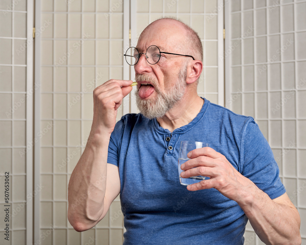 senior man is taking a medicine or supplement pill with a glass of water at home, self care health concept senior man is taking a medicine or supplement pill with a glass of water at home, self care health concept