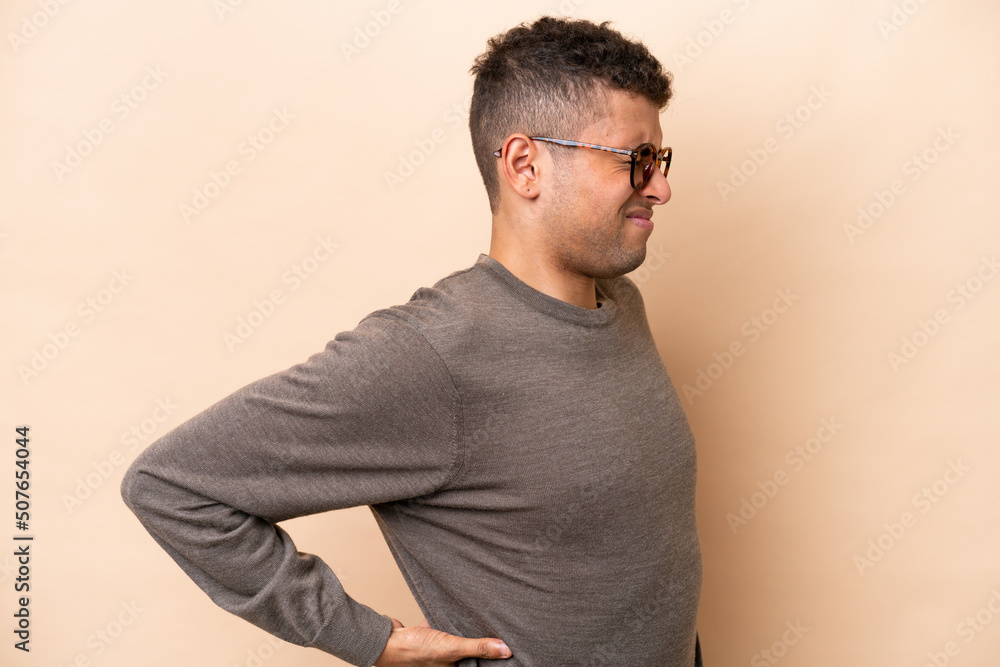 Young Brazilian man isolated on beige background suffering from backache for having made an effort Young Brazilian man isolated on beige background suffering from backache for having made an effort