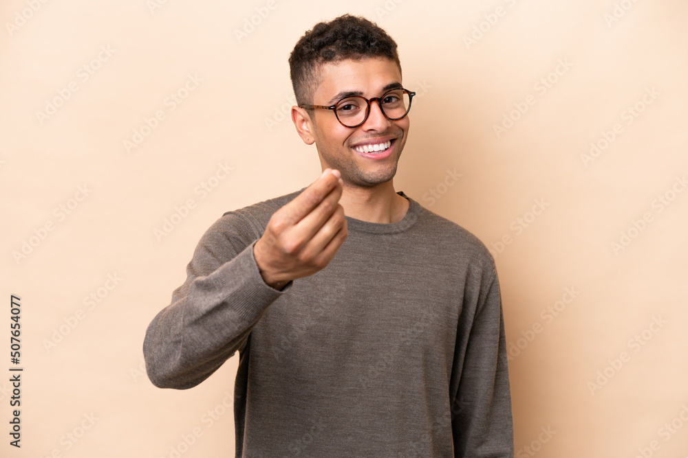 Young Brazilian man isolated on beige background making money gesture Young Brazilian man isolated on beige background making money gesture