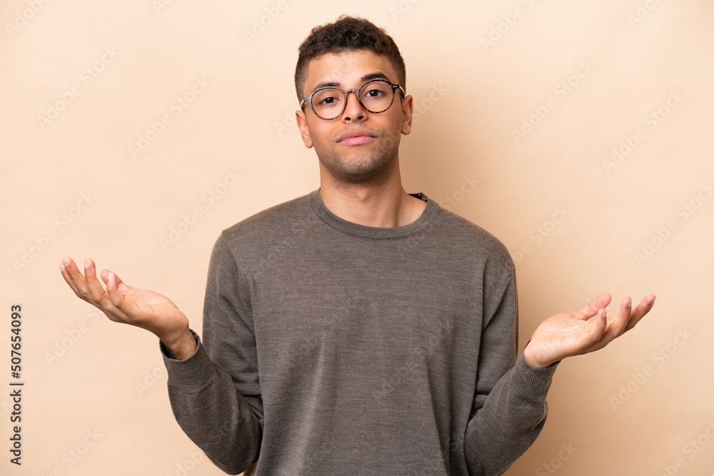 Young Brazilian man isolated on beige background having doubts Young Brazilian man isolated on beige background having doubts