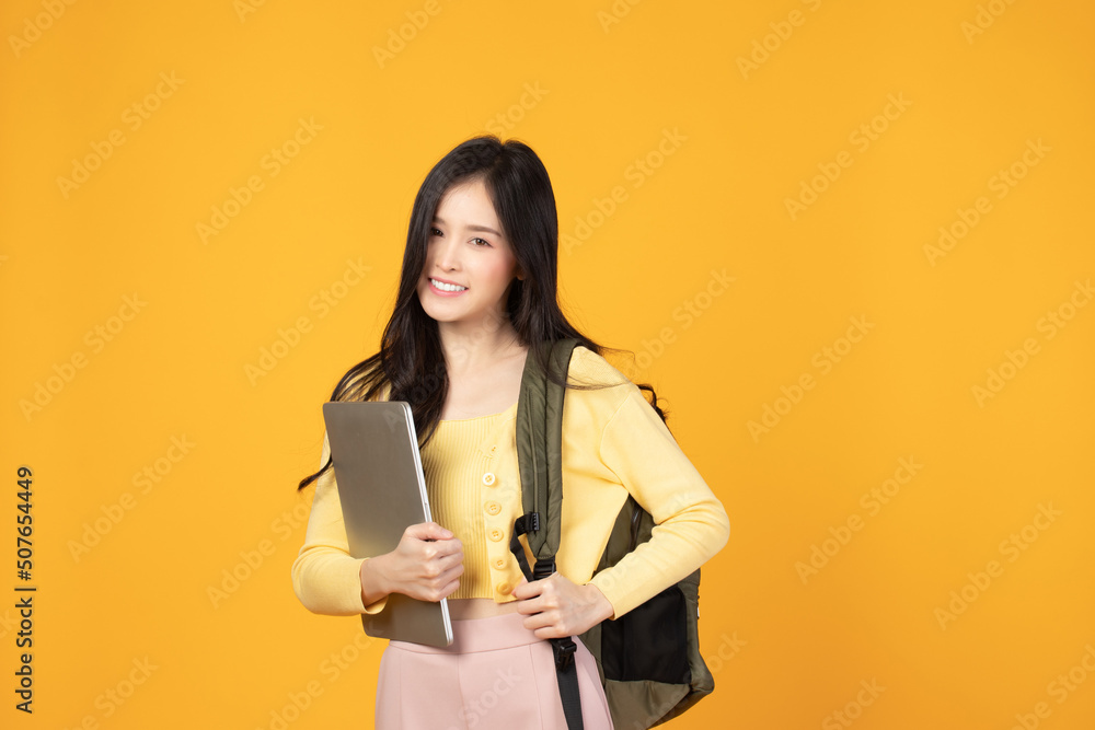 Portrait of happy casual Asian girl student with backpack and laptop isolated on yellow background. Back to school and learning concept. Portrait of happy casual Asian girl student with backpack and laptop isolated on yellow background. Back to school and learning concept.