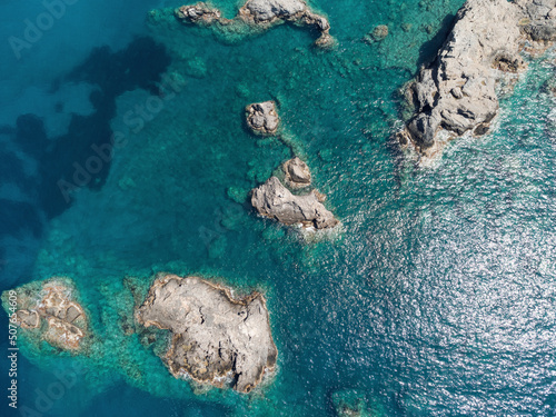 Aerial top view of sea waves hitting rocks on the beach with turquoise sea water. Sea waves on the wild rocky coast. Seascape. Travel concept. Aegean Sea, Turkey. Postcard view. Drone shot