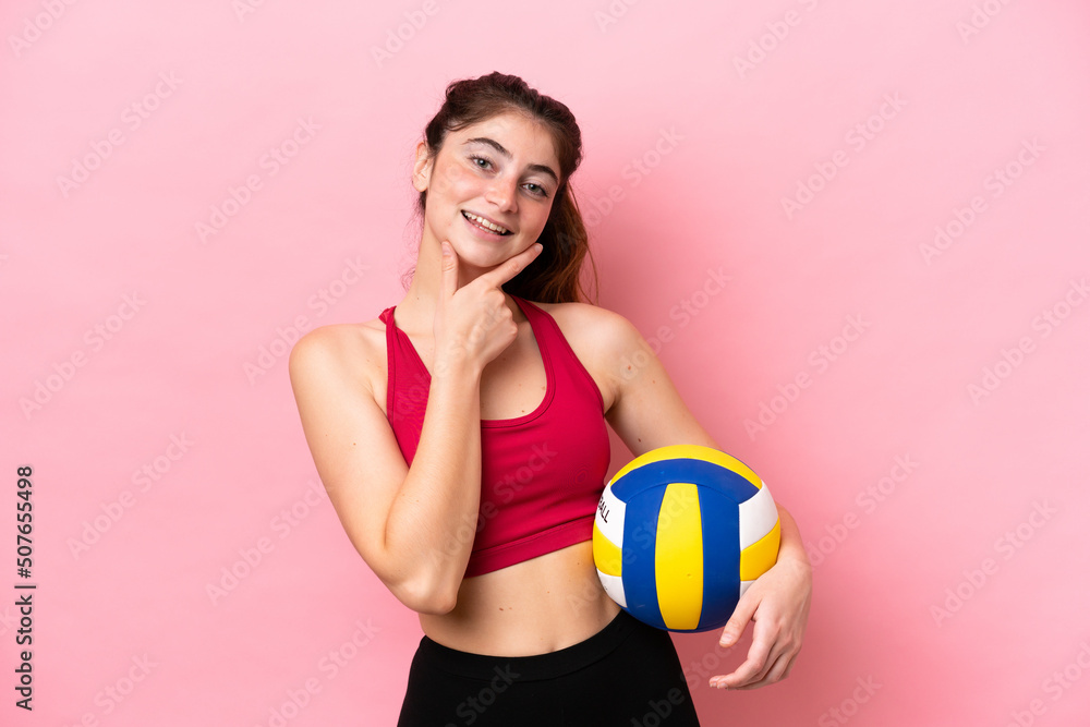 Young caucasian woman playing volleyball isolated on pink background happy and smiling