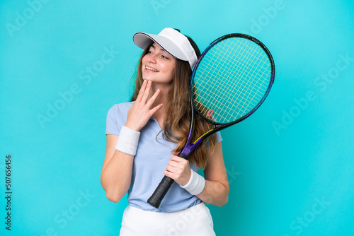 Young tennis player woman isolated on blue background looking up while smiling