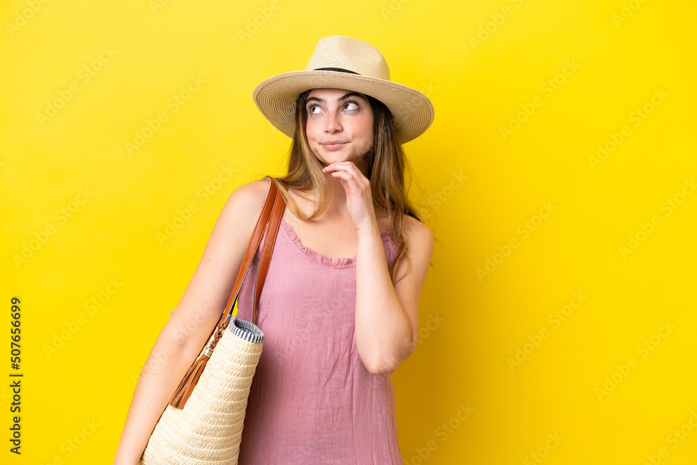 Young caucasian woman holding a beach bag isolated on yellow background and looking up Young caucasian woman holding a beach bag isolated on yellow background and looking up