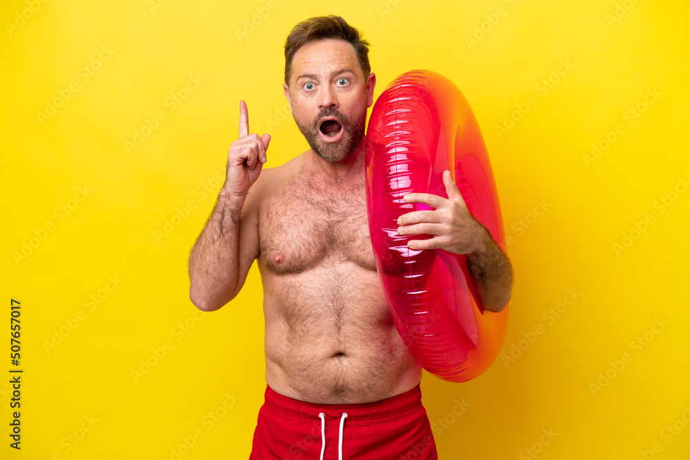 Middle age caucasian man holding inflatable donut isolated on yellow background thinking an idea pointing the finger up