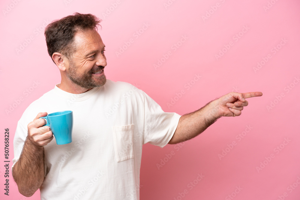 Middle age caucasian man holding cup of coffee isolated on pink background pointing to the side to present a product Middle age caucasian man holding cup of coffee isolated on pink background pointing to the side to present a product