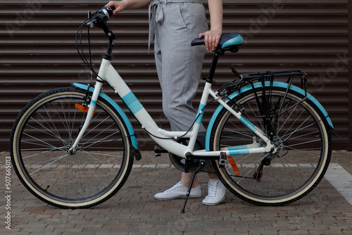 White bicycle stands in yard. Behind female legs in trousers