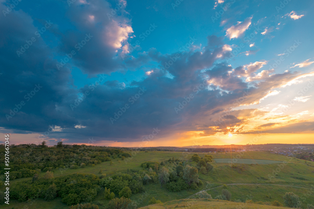 Stunning sunset sky with clouds over green hills. Summer countryside view.