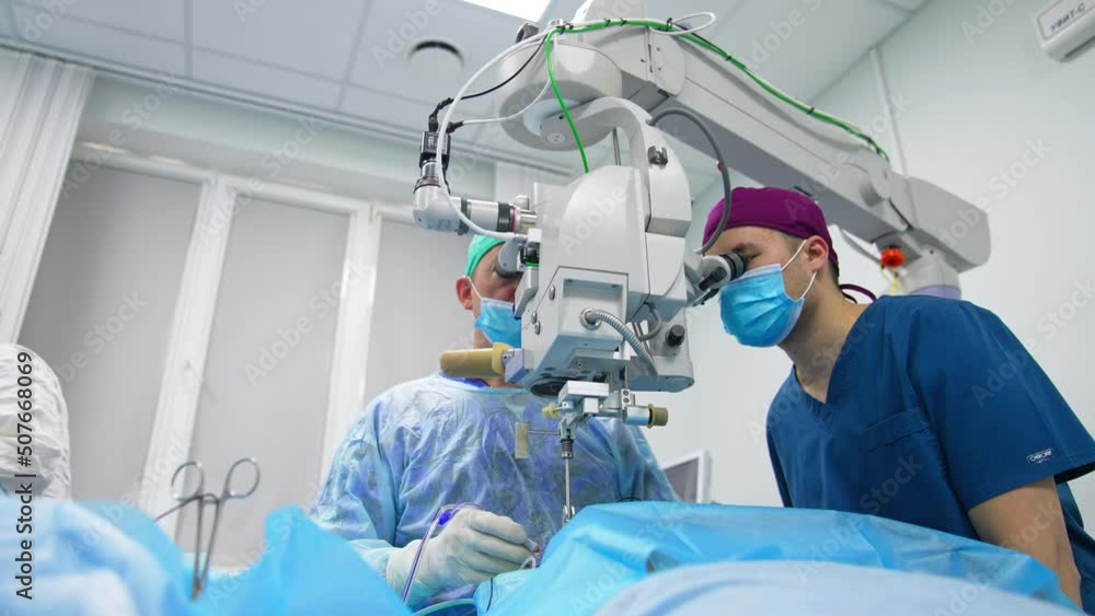 Delicate eyesight operation in modern hospital. Two doctors use microscope to perform ophthalmic surgery. Low angle view. Delicate eyesight operation in modern hospital. Two doctors use microscope to perform ophthalmic surgery. Low angle view.