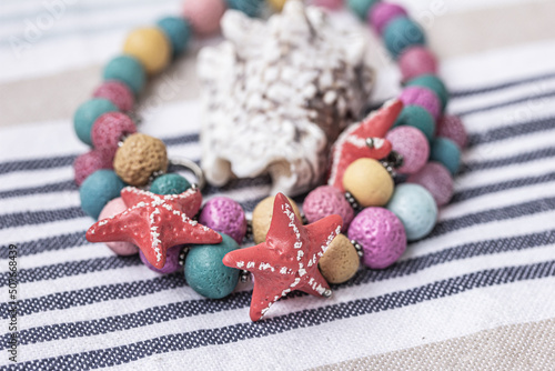 Womens Bracelet made of beads, seahell, red sea stars on striped marine background, travel, sea vacation, summer time concept.