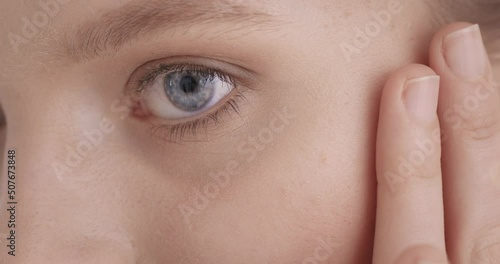Face skin care. Charming female model with perfect healthy skin doing massage with fingers under eyes. Young caucasian woman enjoying beauty routine in studio. Close up.